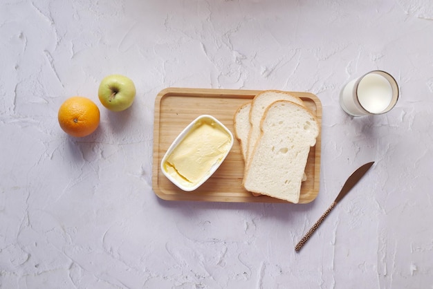 Mantequilla fresca en un recipiente con leche de pan y manzana en la mesa