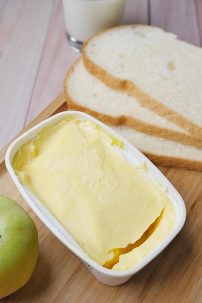 Mantequilla fresca en un recipiente con pan sobre fondo blanco.