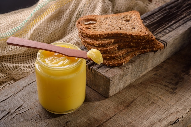 Mantequilla de ghee en frasco de vidrio con espátula de madera y pan de molde en la mesa de madera