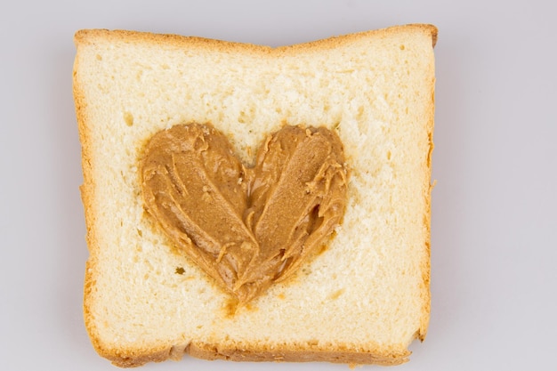 Mantequilla de maní casera y sándwich en forma de corazón sobre fondo blanco El concepto de amor por la comida Desayuno favorito