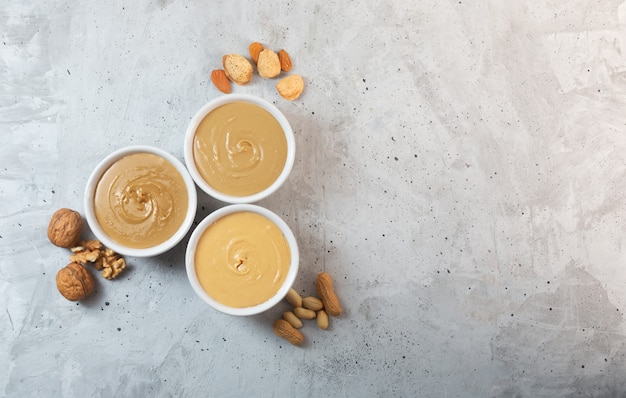 Mantequilla de maní, nueces y almendras en la mesa gris, vista superior, espacio de copia