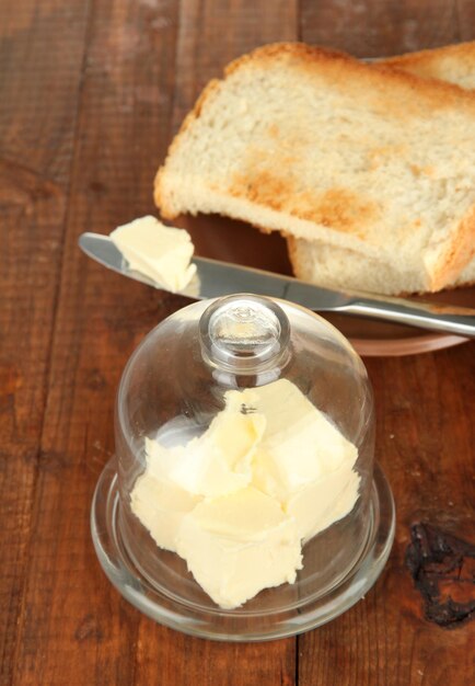 Foto mantequilla en plato de vidrio con tapa de vidrio y pan fresco sobre fondo de madera