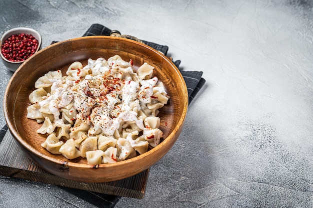 Manti-Dumpling mit Joghurt und Tomatensauce auf einem Holzteller Weißer Hintergrund Top-View Kopierraum