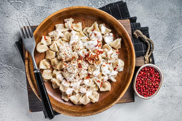 Manti Dumpling mit Joghurt und Tomatensauce in einer Holzplatte Weißer Hintergrund Ansicht von oben