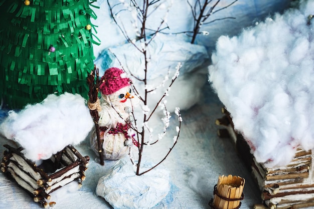 Manualidades infantiles del patio de invierno en la nieve: casa, árboles, pozo, muñeco de nieve.