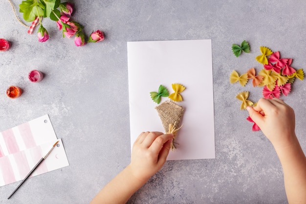 Manualidades en papel para el día de la madre, 8 de marzo o cumpleaños. Niño pequeño haciendo un ramo de flores de papel de colores y pasta de colores.