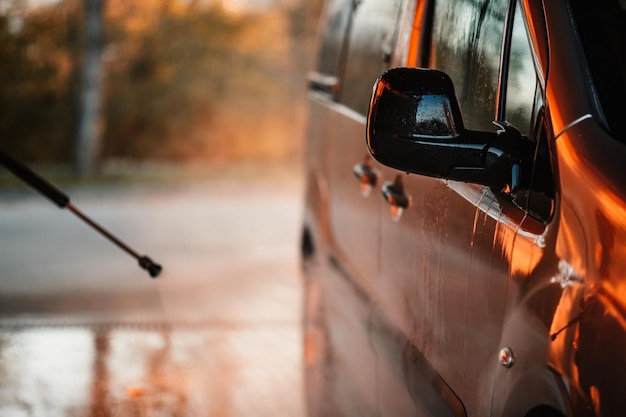 Manuelle Autowäsche mit weißem Seifenschaum auf der Karosserie Autowäsche mit Hochdruckwasser