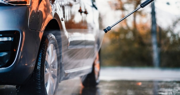 Manuelle Autowäsche mit weißem Seifenschaum auf der Karosserie Autowäsche mit Hochdruckwasser