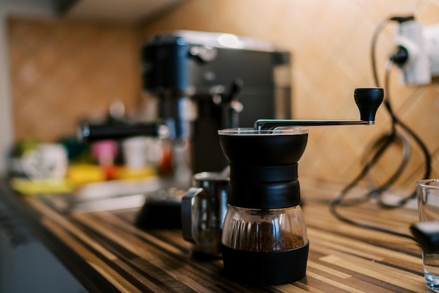 Foto manuelle kaffeemühle mit gemahlenem kaffee steht auf dem tisch in der nähe der kaffeemaschine