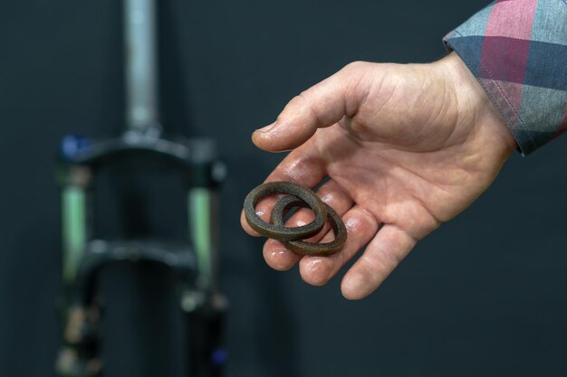 Manutenção de um moderno garfo absorvente de choque e substituição de retentores de óleo Reparação de bicicleta de montanha em uma oficina profissional Partes do garfo na mão do mecânico em um fundo preto