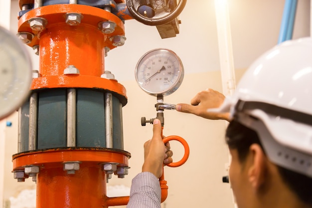 Manutenção do engenheiro asiático verificando dados técnicos do equipamento do sistema condensador bomba de água e manômetro, bomba de água do chiller com manômetro.