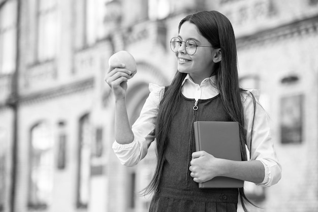 Manzana al día mantiene al médico alejado Niño pequeño sostiene manzana y libro al aire libre Merienda de manzana Merienda escolar Comida y dieta saludables Alimentación orgánica y natural Educación para la salud Manera correcta de tomar vitaminas