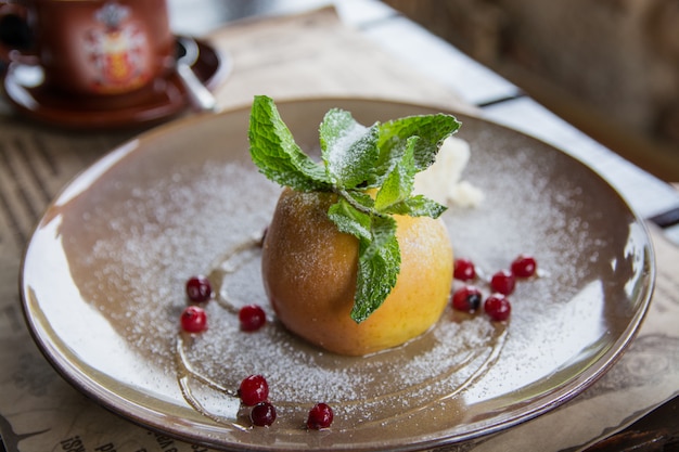 La manzana al horno con helado y menta en un plato de cerámica. Postres utiles.