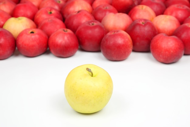 Manzana amarilla en una de manzanas rojas sobre blanco