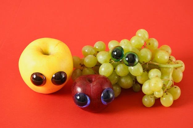 Manzana de ciruela y racimo de uvas con ojos de marioneta concepto de broma fondo rojo caras de frutas lindas