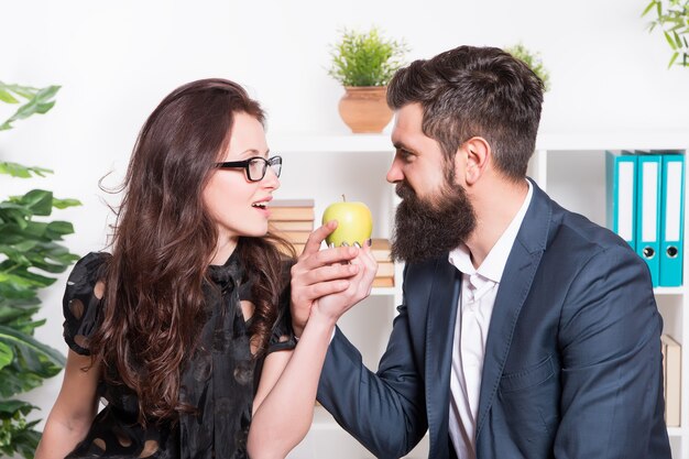 La manzana es rica en vitaminas. Jefe y secretaria sensual con frutas de vitamina en la oficina. Hombre barbudo y mujer sexy con bocadillos saludables de vitamina en el trabajo. Los alimentos vitamínicos realmente funcionan.