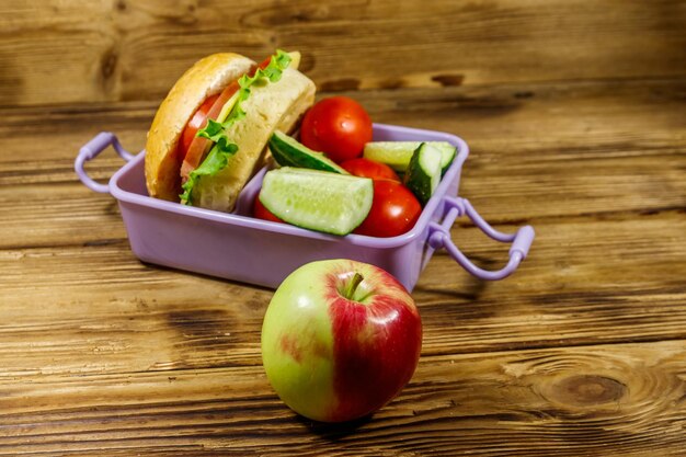 Manzana y fiambrera con hamburguesas y verduras frescas en una mesa de madera