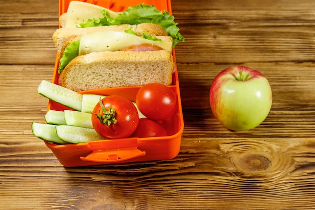 Manzana y fiambrera con sándwiches y verduras frescas en una mesa de madera