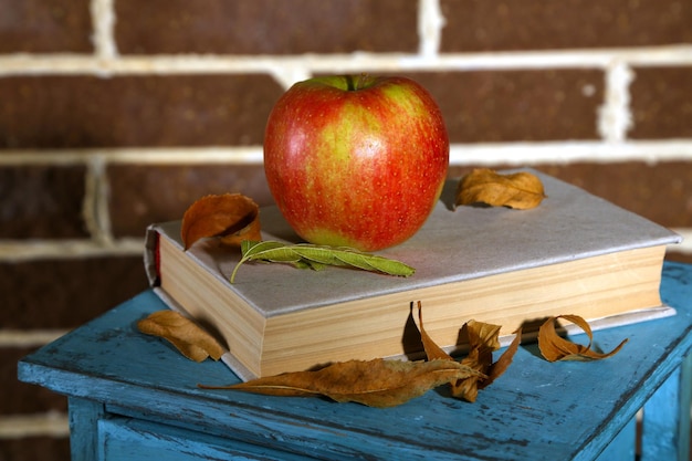Manzana con libros y hojas secas sobre soporte de madera sobre fondo de ladrillo