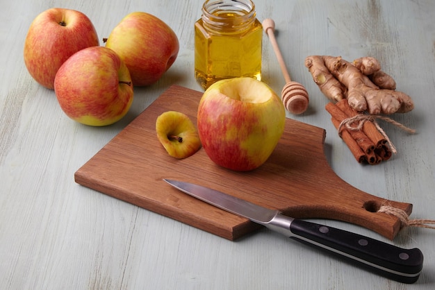 Manzana preparada para hornear en el horno rodeada de ingredientes con miel, canela y jengibre, se encuentra sobre una mesa de madera azul