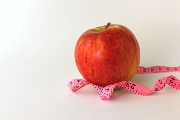 Manzana roja y cinta métrica sobre un fondo blanco.