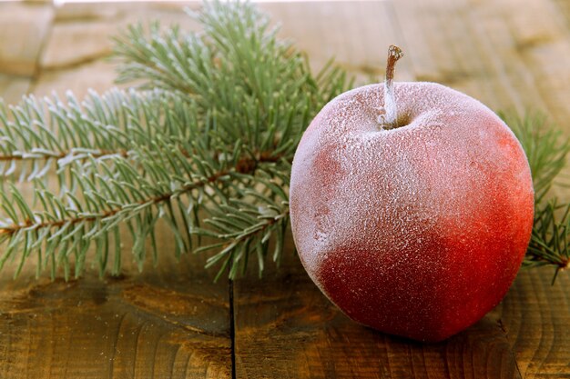 Manzana roja esmerilada con rama de abeto en mesa de madera