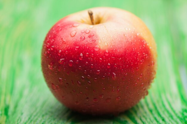 Manzana roja fresca con gotas de agua sobre fondo de madera verde con textura brillante