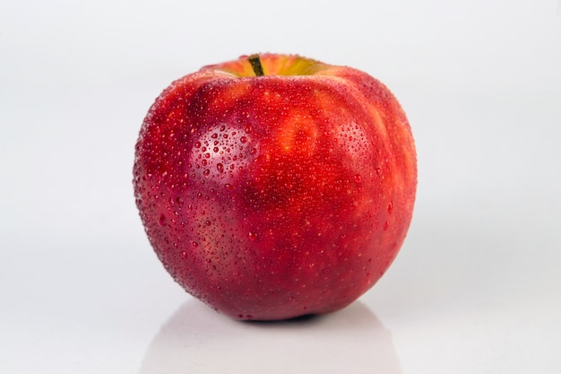 Manzana roja fresca con gotas de agua sobre una superficie blanca con reflejo.