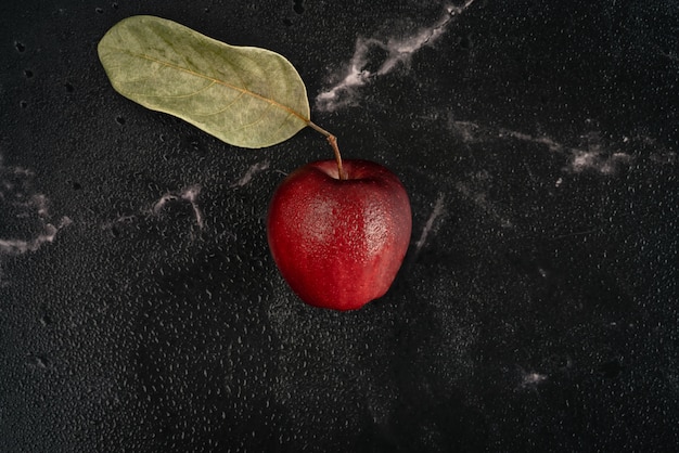 Manzana roja fresca con hojas verdes y gotas de agua se encuentra sobre un fondo de mármol negro lleno de gotas de spray de agua. Vista superior composición plana laico.