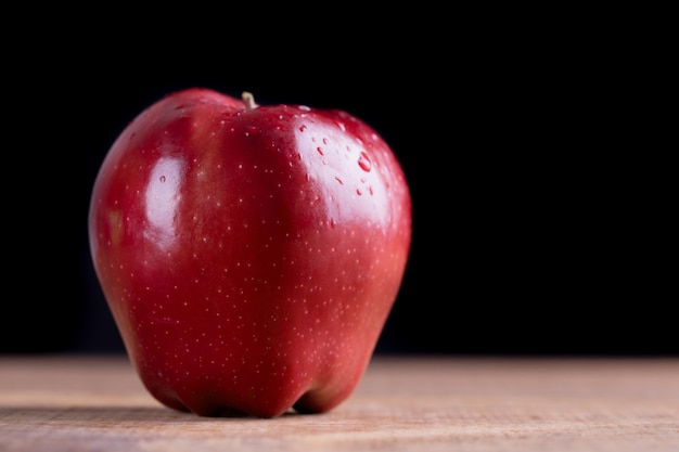 Manzana roja con gota de agua en la mesa de madera.