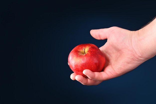Manzana roja en la mano del hombre sobre un fondo oscuro.