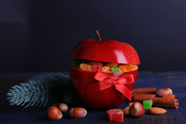 Manzana roja rellena de frutos secos con canela, ramita de abeto y avellana sobre mesa de madera de color y fondo oscuro