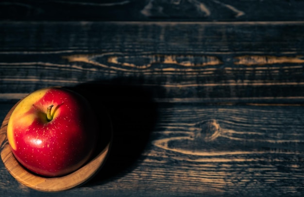 Una manzana roja sobre una mesa de madera con un cuenco de madera sobre la mesa