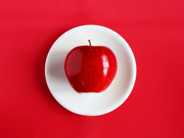 Manzana roja sobre un plato blanco, sobre un fondo rojo.