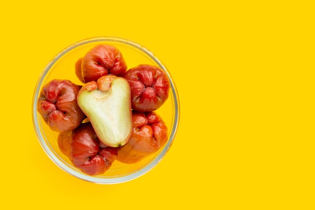 Manzana rosa fresca en un tazón de vidrio sobre fondo amarillo.