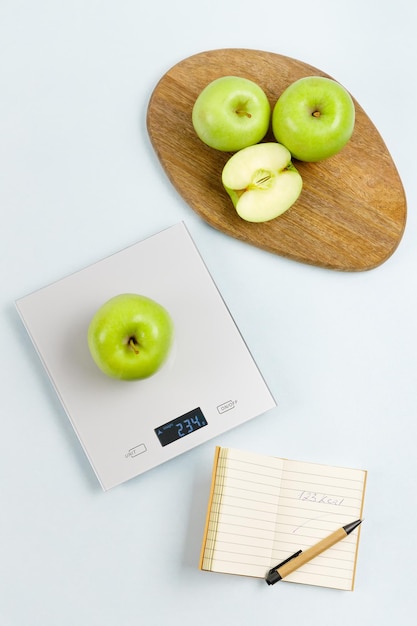 manzana verde en básculas de cocina Cerca del bloc de notas con el número de calorías y algunas manzanas a bordo