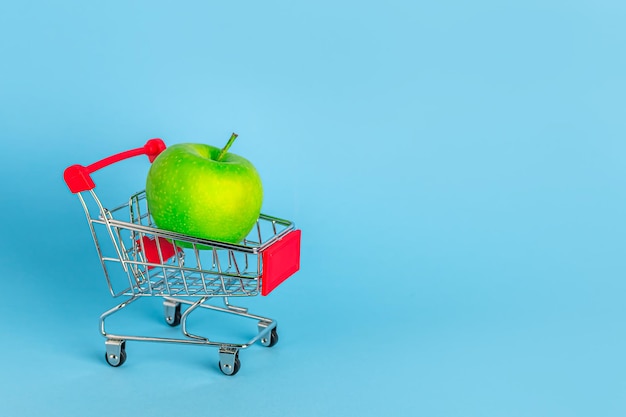 Manzana verde en un carrito de compras sobre un fondo azul con espacio para copiar