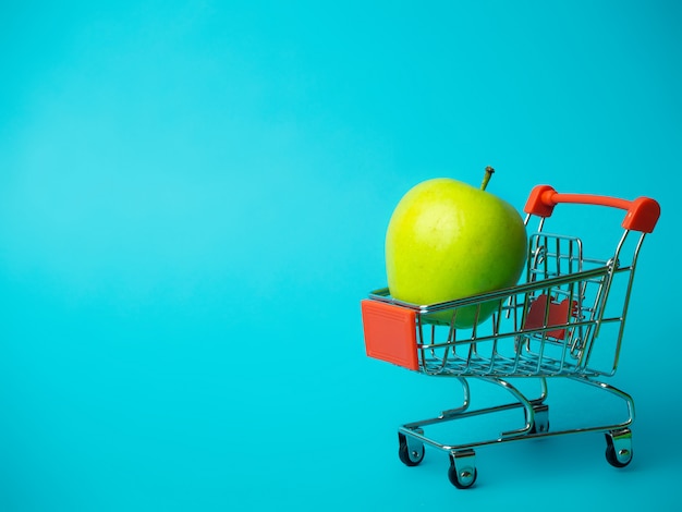 Manzana verde en un carro sobre un fondo azul.