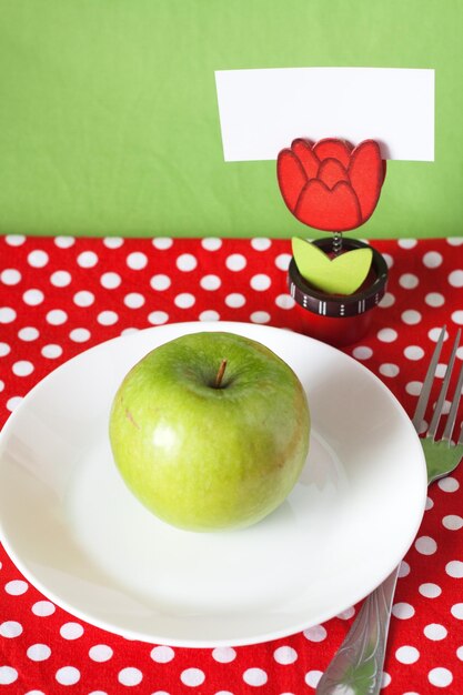 La manzana verde se encuentra en un plato blanco sobre un fondo de lunares rojos junto a una pinza para la ropa con una nota en