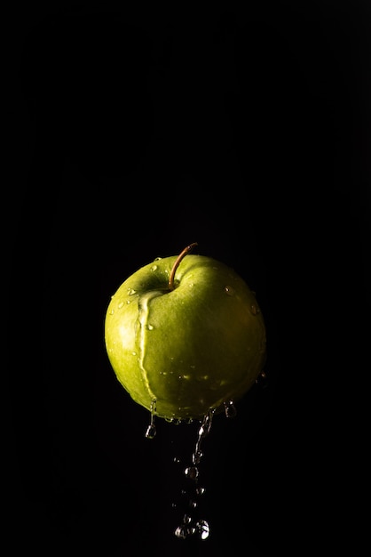 Manzana verde con hermosas salpicaduras de agua con fondo negro y enfoque selectivo.