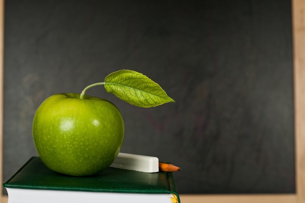 Manzana verde con hoja contra la pizarra en clase. Concepto de escuela