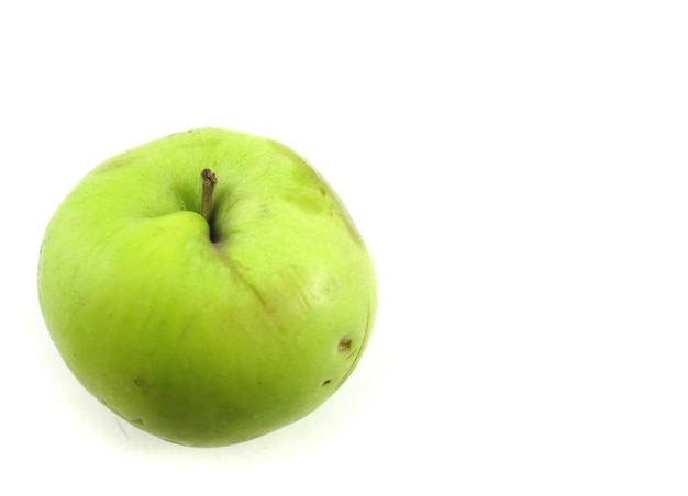 Una manzana verde con un lado podrido de caer sobre un fondo blanco. Fruta.