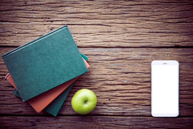 Manzana verde, libros con teléfono celular en el fondo de madera.