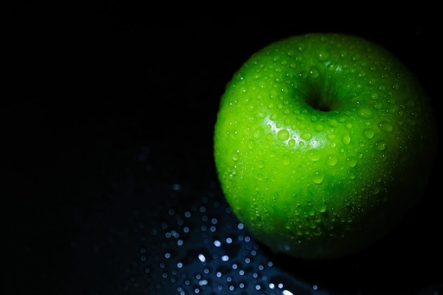 Manzana verde madura con gotas de agua en un primer plano de fondo negro