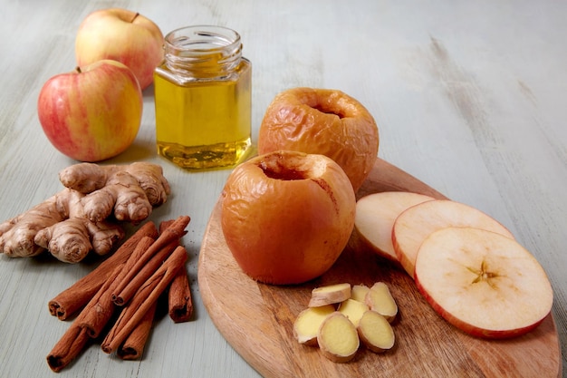 Manzanas al horno con miel, jengibre y canela rodeadas de ingredientes sobre una mesa de madera clara. Vista frontal con espacio de copia.