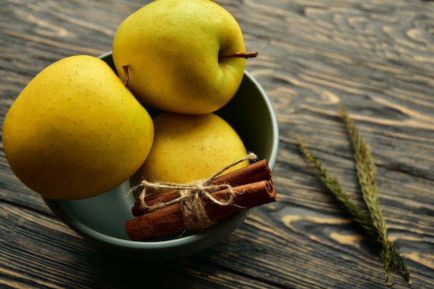 Manzanas amarillas de árbol y palitos de canela en un recipiente sobre un fondo oscuro de la madera. Vista lateral. Naturaleza muerta.