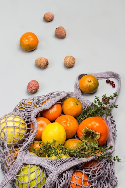 Manzanas de caqui y limón en bolsas de malla reutilizables Lychee arándanos y mandarinas en la mesa