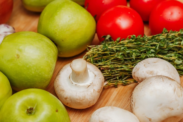 Manzanas, champiñones, hierbas y verduras sobre tabla de madera.