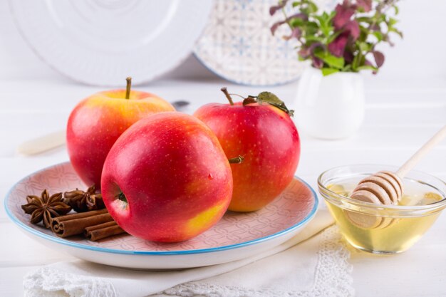 Manzanas dulces orgánicas frescas y maduras en un plato con ramas de canela, estrellas de anís y miel sobre una mesa de cocina blanca.