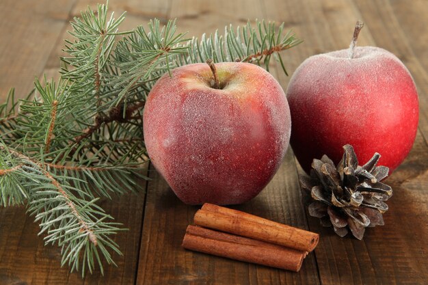 Manzanas esmeriladas rojas con rama de abeto y protuberancias sobre fondo de madera